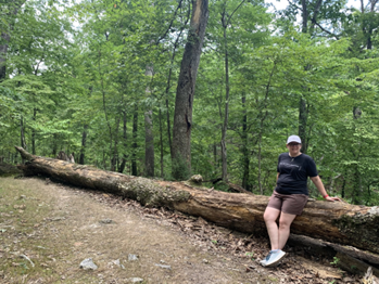 Kara sits on a fallen tree trunk in a lush wooded area.