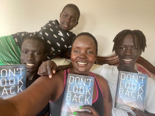 Achut Deng and her three sons pose on a couch, smiling. Achut and two of the sons are each holding a copy of Don't Look Back.