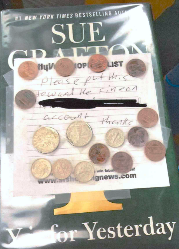 A library book has a note and many coins taped to the cover. The note says, 