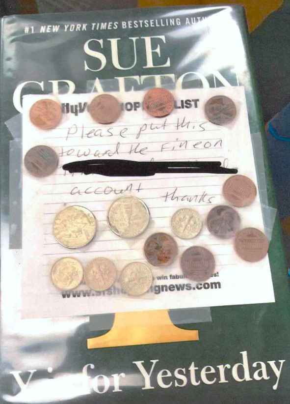 A library book has a note and many coins taped to the cover. The note says,
