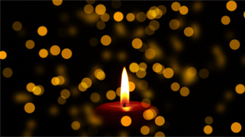 A candle burns in the darkness, with small twinkling lights surrounding the central flame.