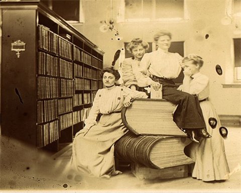 Four librarians in the Sioux Falls Carnegie library pose with giant guest books from the 1893 World's Fair