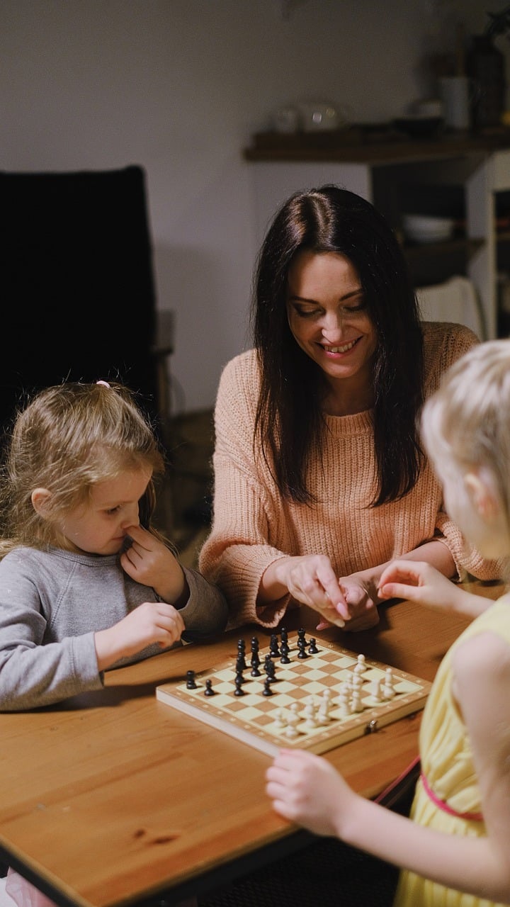 A woman plays chess with two small children.