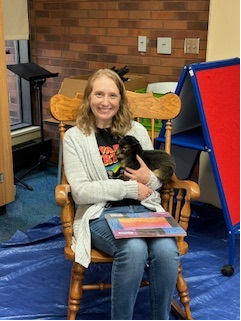 a library staff member sitting with a baby goat and a book