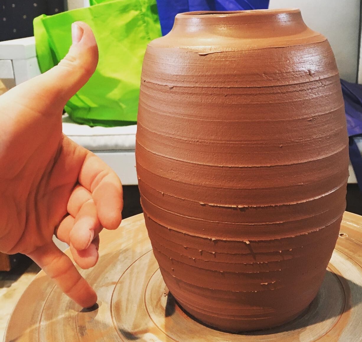 In progress earthenware funerary urn. Hand with thumb and pinky extended next to urn for scale.