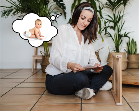 Woman sits on the floor with assembly instructions, thinking about a baby.