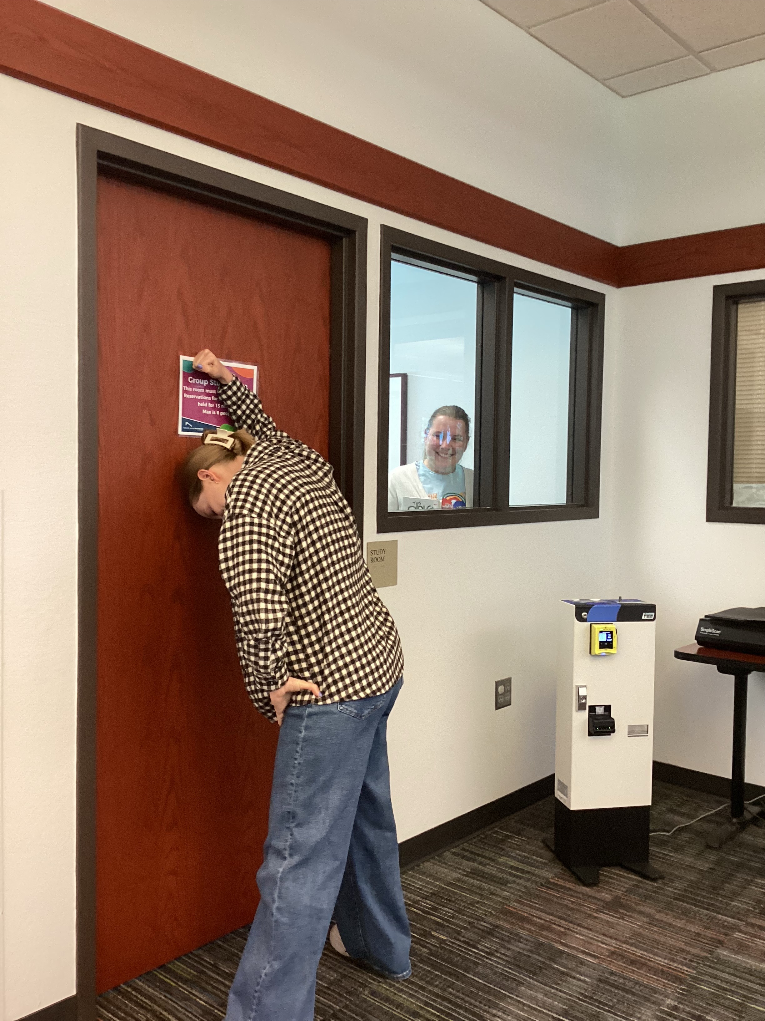One staff member knocks on the Group Study Room door, while another smiling staff looks out at her.