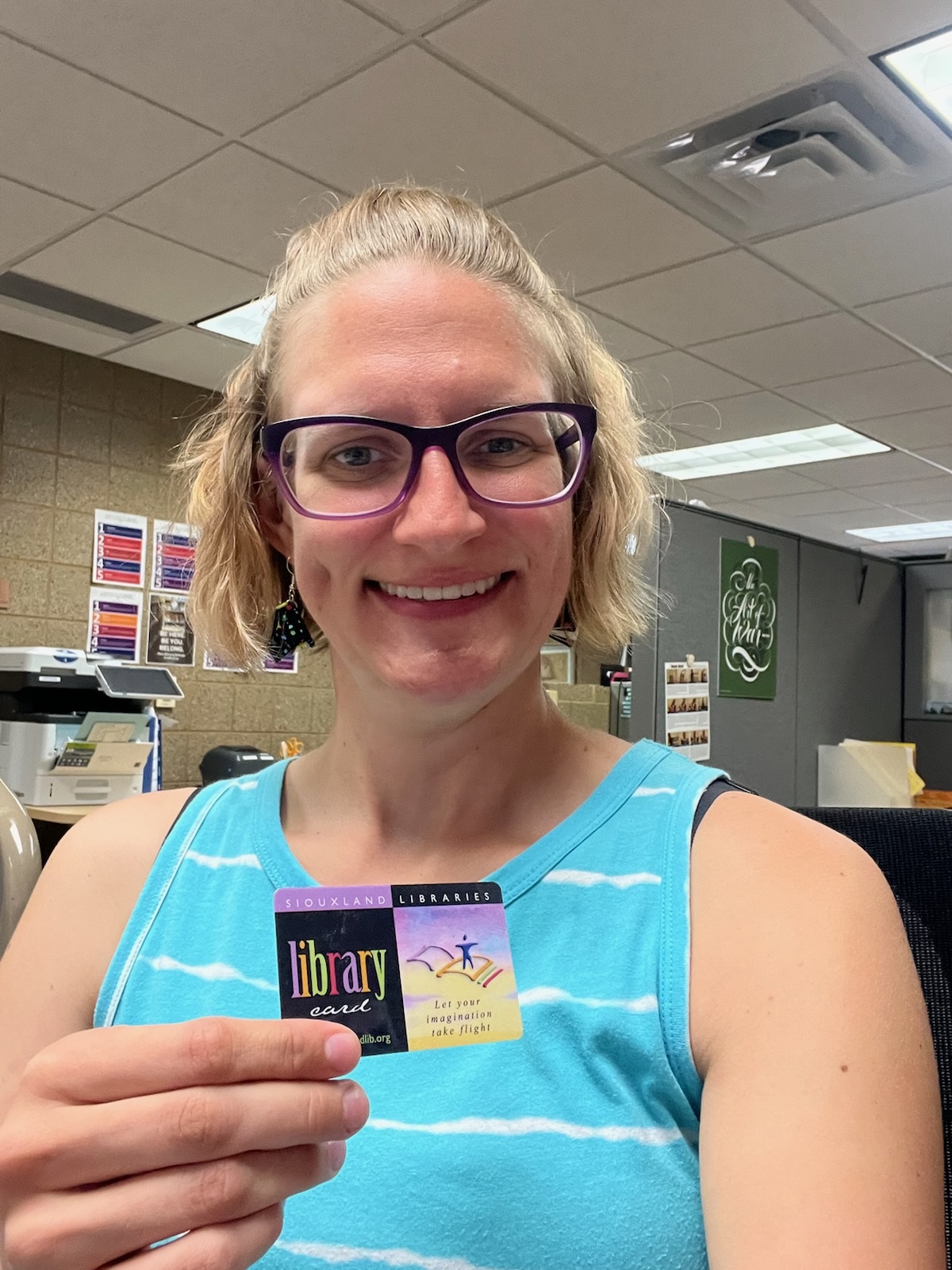 Library Associate Alice smiling seated at her desk holding her personal library card
