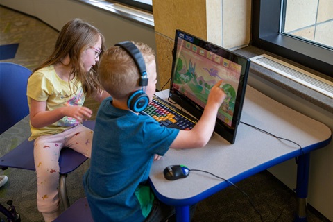 A boy and girl look at an AWE computer screen at the library.