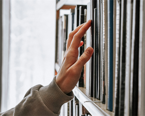 a hand reaching out to touch books on a bookshelf