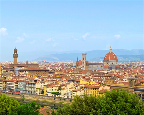 An Italian city skyline in front of foothills obscured by a hazy sunny day.