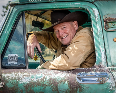 Author Craig Johnson wearing a brown cowboy hat and jacket, sitting in an old teal pick-up truck