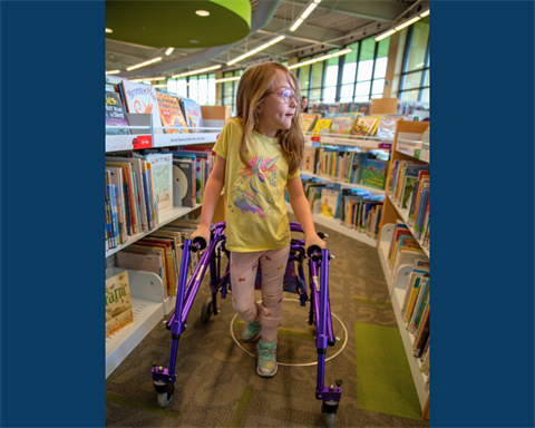 A girl with a walker browses the library's children's books.